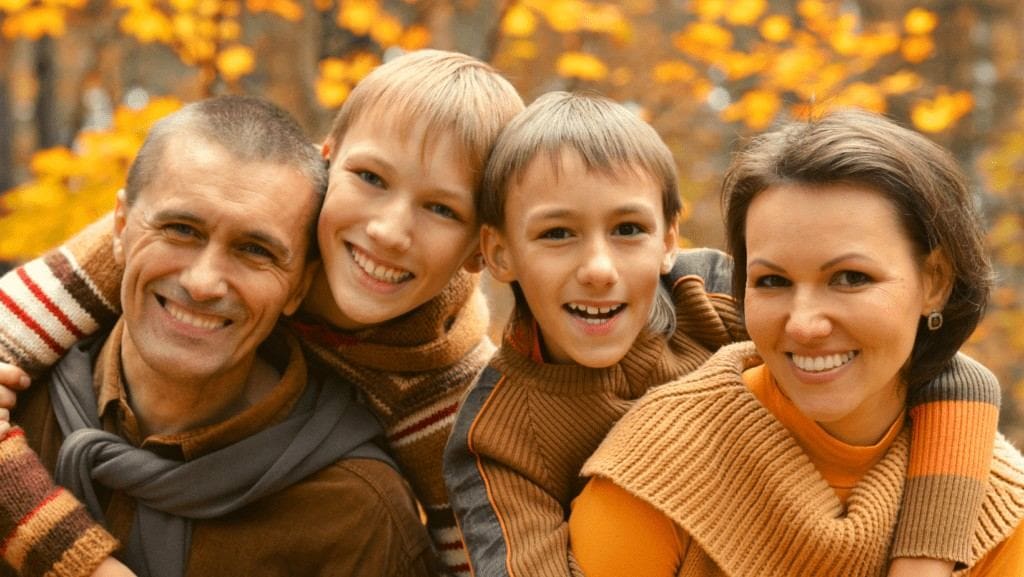 Man and woman with implant dentures in Northampton smiling with their two kids among fall trees