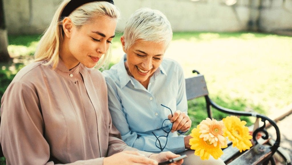 Two women looking at a phone together on a park bench