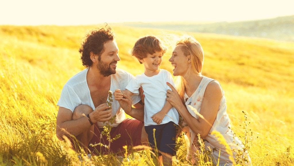 Mother and father sitting in grassy field with their toddler after root canal treatment in Northampton