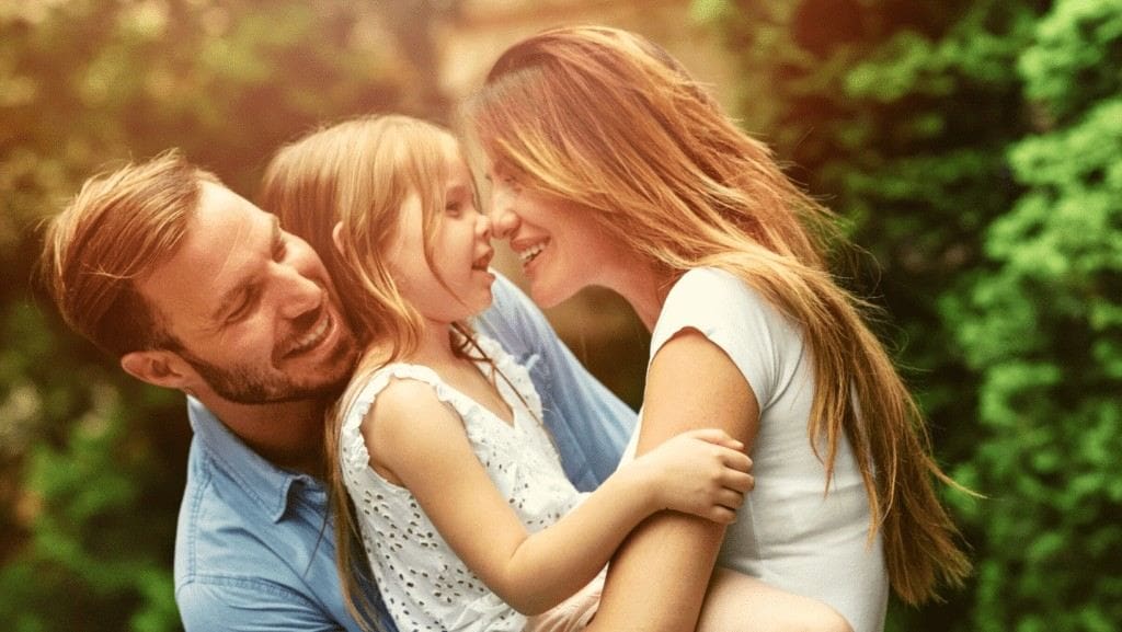 Man and woman laughing with their young daughter outdoors after tooth extractions in Northampton