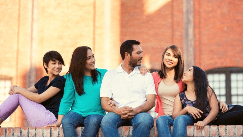 Family of five sitting on red brick ledge in front of building