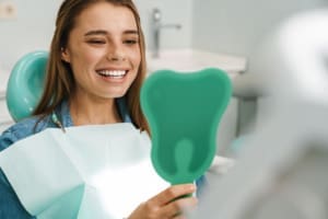 European young woman smiling while looking at mirror in dental clinic