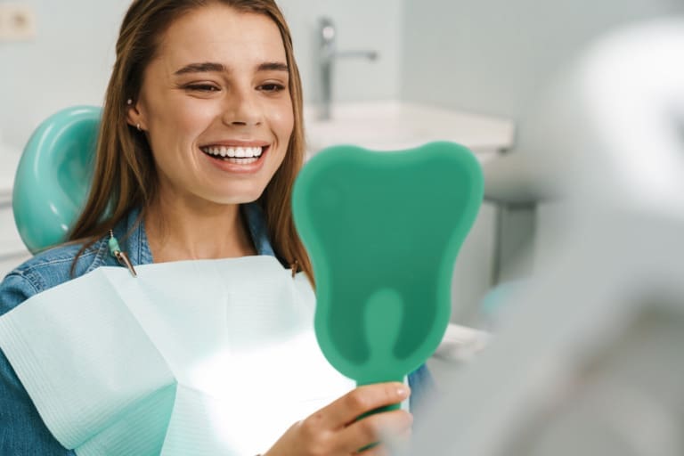 European young woman smiling while looking at mirror in dental clinic