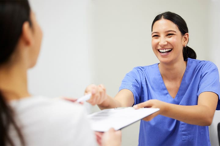 Smiling dental assistant handing patient forms
