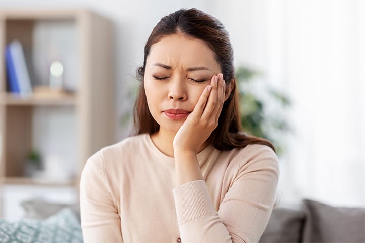Woman in pink shirt rubbing her jaw in pain