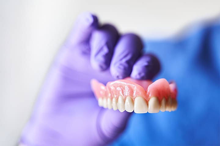 Gloved hand holding a full upper denture