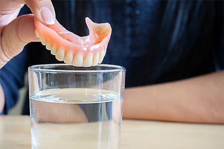 Person placing dentures in a glass of water.