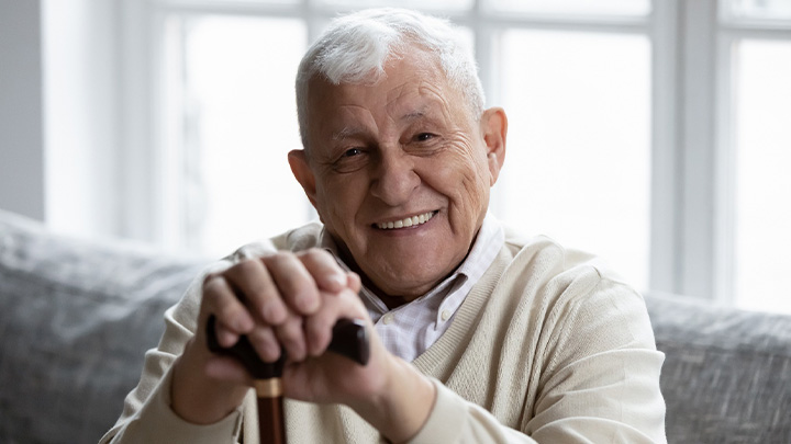 An older, smiling man sitting on a couch.