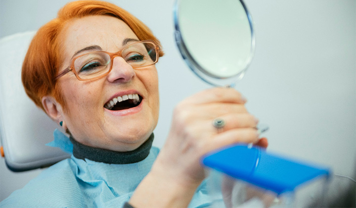 An older woman admiring her smile with a hand mirror.