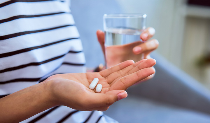 Close-up of person holding pain medication and glass of water.