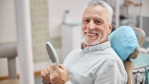 Male patient in dental chair holding mirror and smiling.