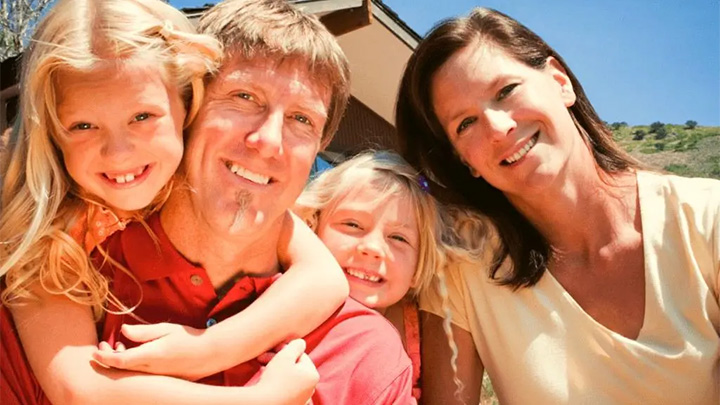 A smiling family poses outdoors under a clear blue sky.