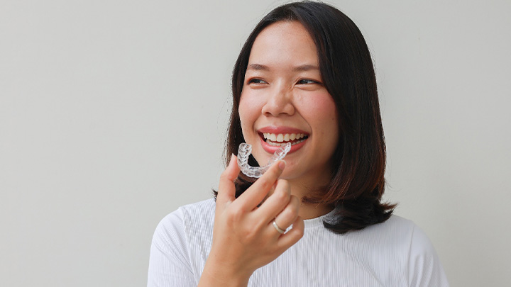 Smiling patient holding clear aligner.