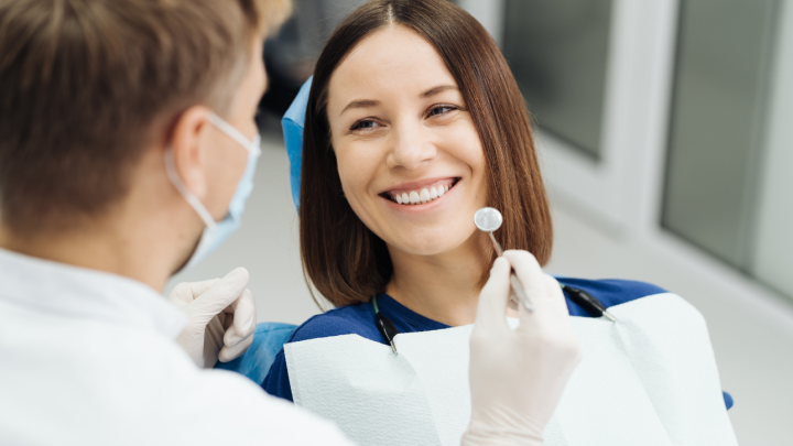 A woman smiles while seated in a dentist's chair, conveying a positive dental experience.