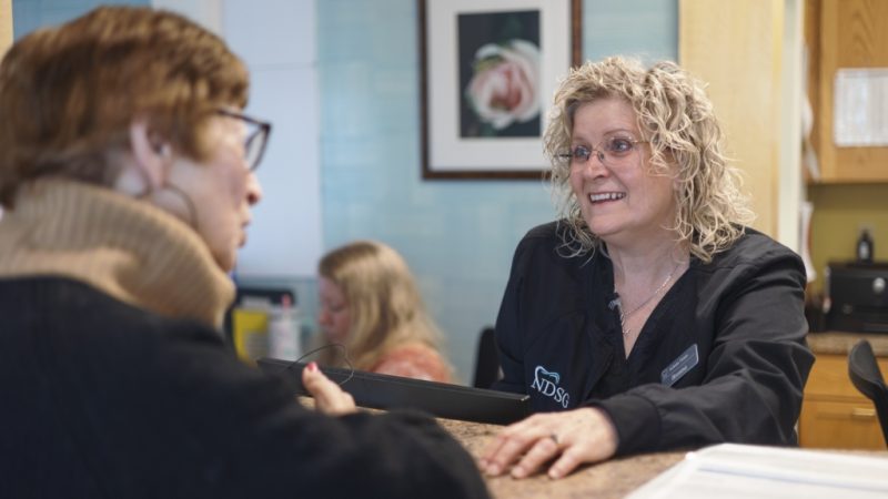 A team member at Northampton Dental Specialists Group converses with another woman in a dental office waiting room, showcasing a friendly atmosphere.