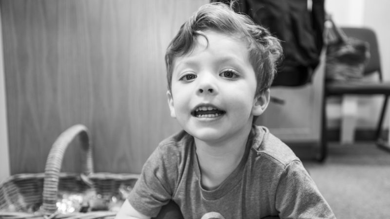 A cheerful young boy sits on the floor, displaying a wide smile, representing a positive dental experience at Northampton Dental Specialists.
